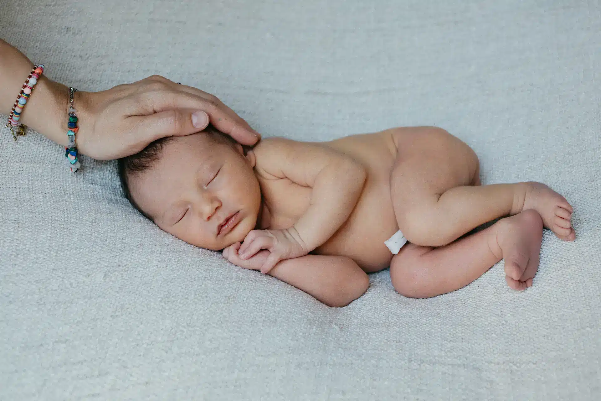 Mains d'une maman posées délicatement sur son nouveau-né endormi, séance photo en studio à Court-Saint-Étienne