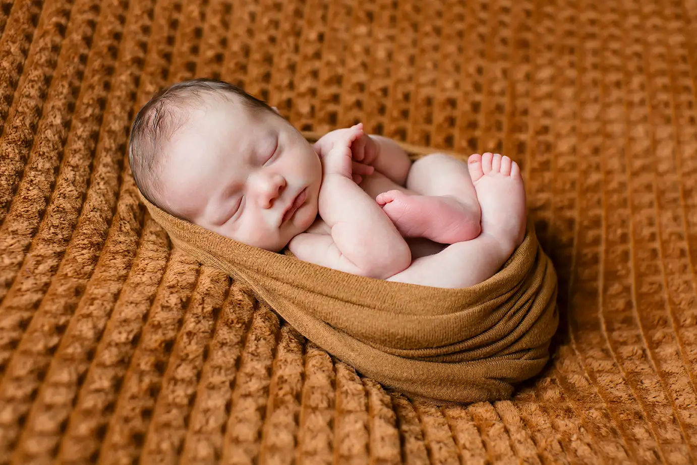 Bébé endormi dans un cocon de tissus doux, séance photo nouveau-né en studio à Court-Saint-Étienne