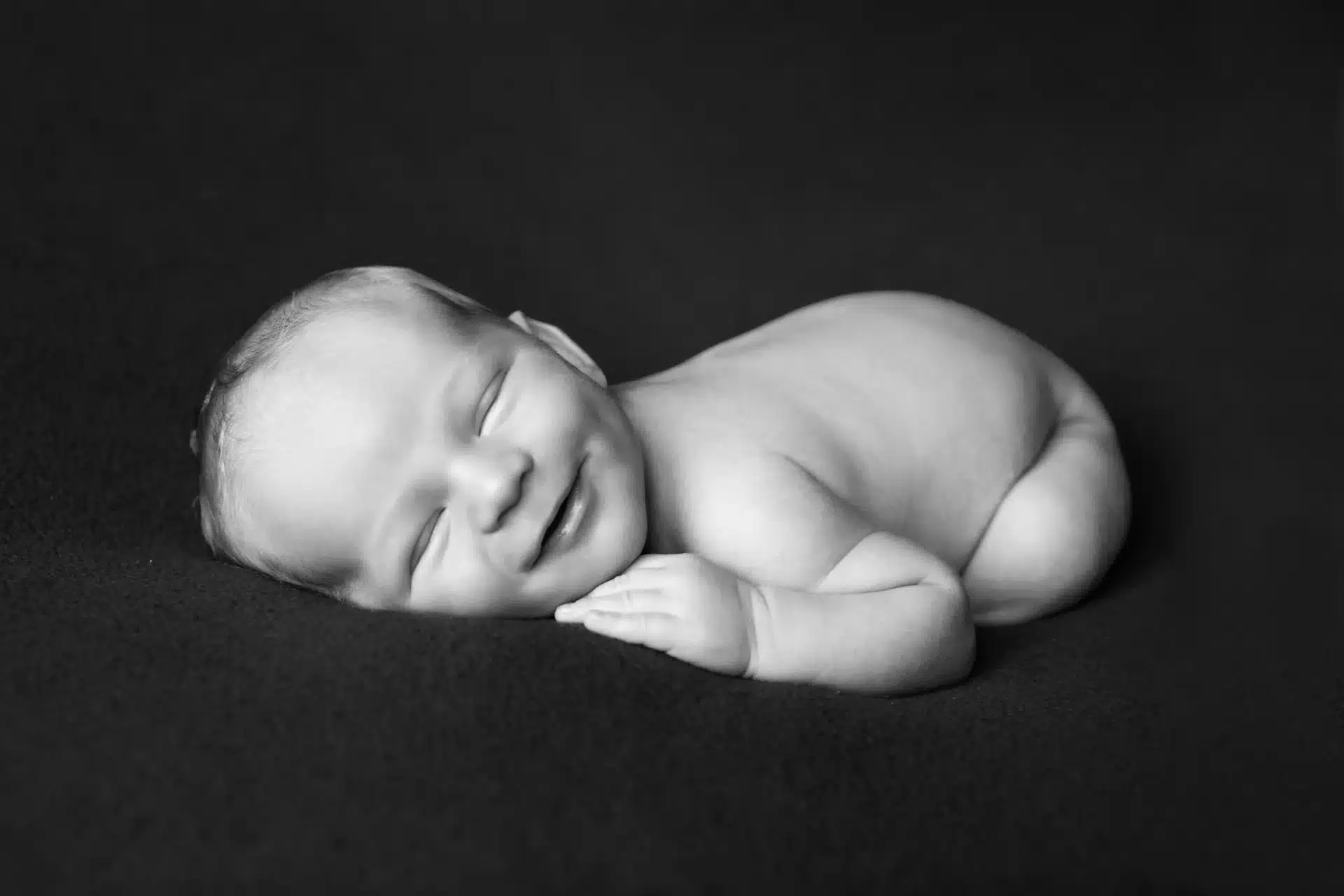 Nouveau-né souriant dans son sommeil, instant de grâce capturé en studio à Court-Saint-Étienne - photographie en Noir et blanc.