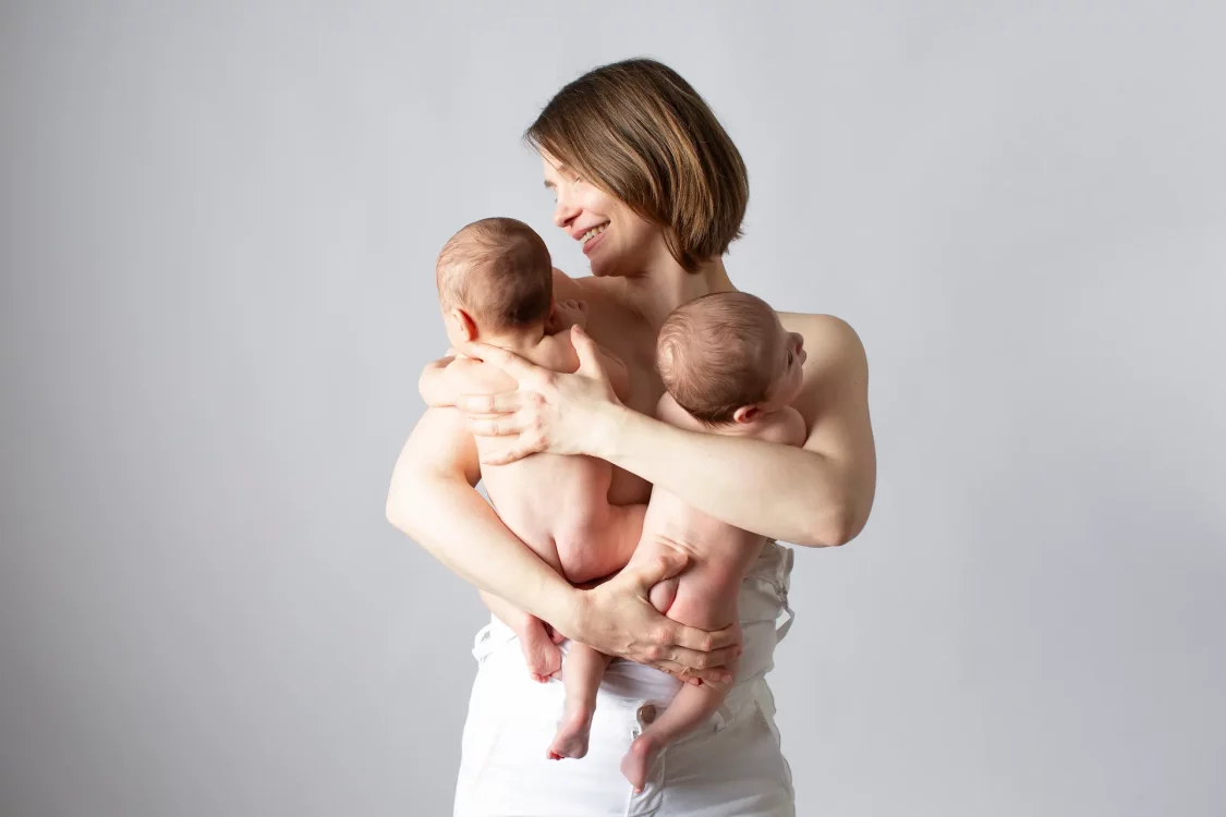 Maman tenant tendrement ses jumeaux nouveau-nés dans les bras, séance photo en studio à Court-Saint-Étienne