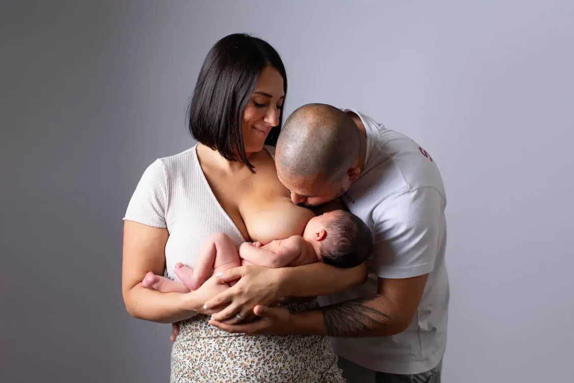 Maman allaitant son bébé et regardant son homme avec amour, séance photo nouveau-né en studio à Court-Saint-Étienne