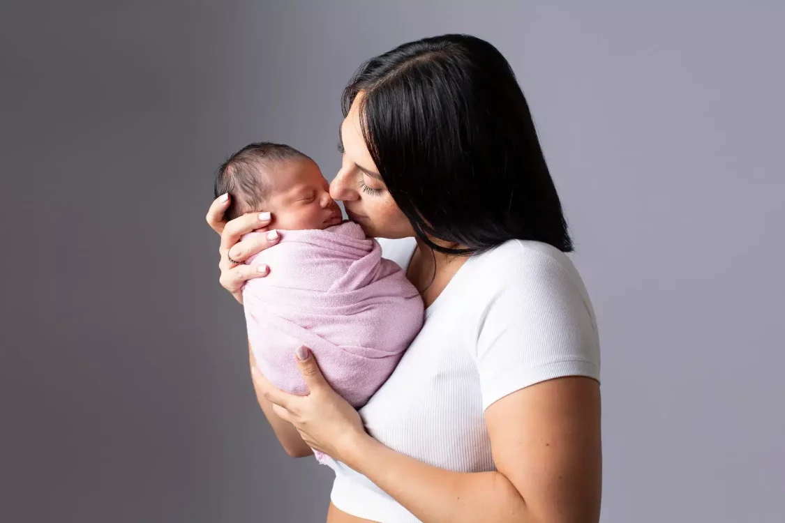 Maman contemplant son bébé endormi contre elle, regard rempli d'amour, studio photo nouveau-né Brabant Wallon
