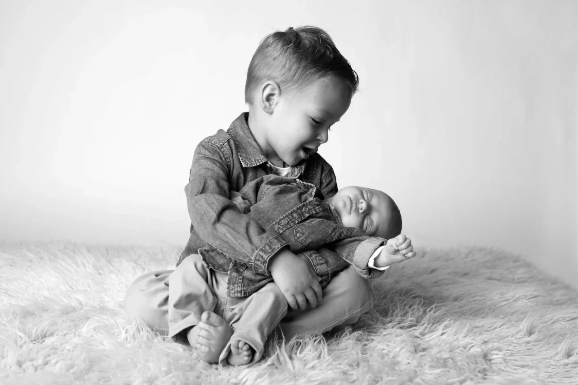 Grand frère portant son petit frère nouveau-né avec émerveillement et fierté séance photo en studio